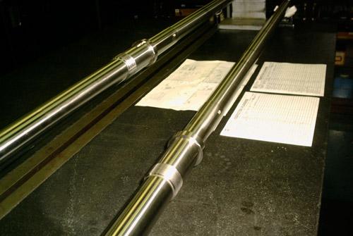 Long CNC manufactured shafts laid out with their inspection paperwork.