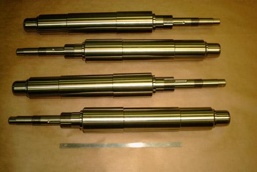 Four finished CNC manufactured shafts laid out for inspection.